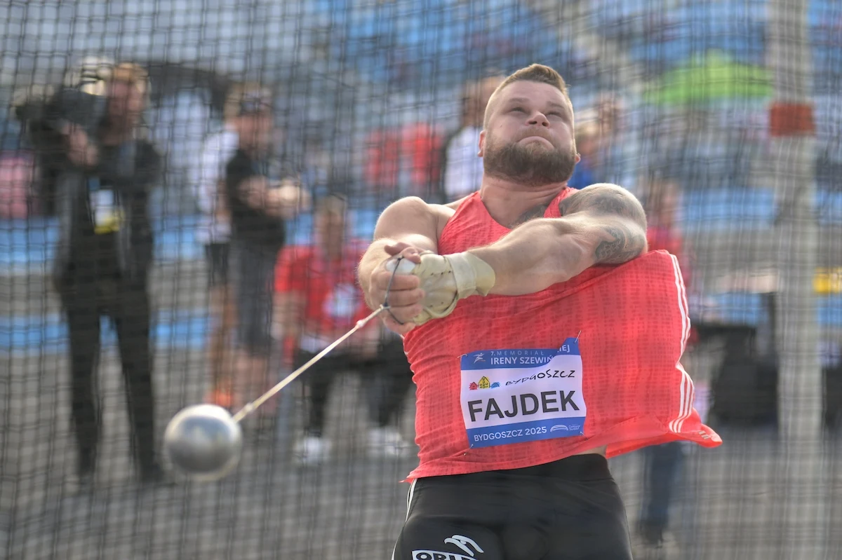 Paweł Fajdek zawodnik wykonujący rzut młotem na stadionie lekkoatletycznym, ujęcie dynamiczne, młot w połowie obrotu, siatka ochronna w tle, publiczność w rozmytym tle