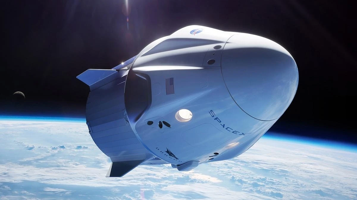 Crew Dragon C213. Tym statkiem Sławosz Uznański-Wiśniewski leci na ISS. Kapsuła załogowa SpaceX Dragon unosząca się nad Ziemią na tle granatowej przestrzeni kosmicznej, widoczne logo NASA oraz amerykańska flaga, szeroka panorama błękitnej planety z lekko zakrzywionym horyzontem.