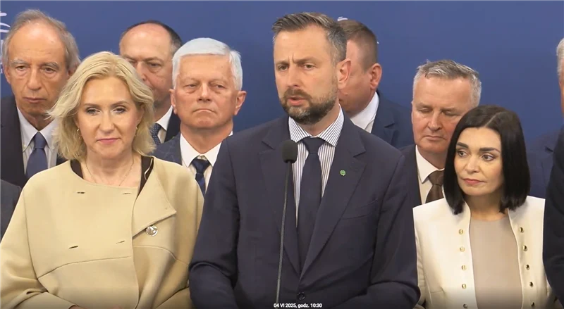 Władysław Kosiniak-Kamysz będzie renegocjował umowę koalicyjną Grupa elegancko ubranych osób stoi przed mikrofonem na tle niebieskiej ścianki, centralną postacią jest mężczyzna w garniturze, po bokach znajdują się kobiety i inni mężczyźni, wszyscy skupieni, wyglądają na zaangażowanych w oficjalne wystąpienie.