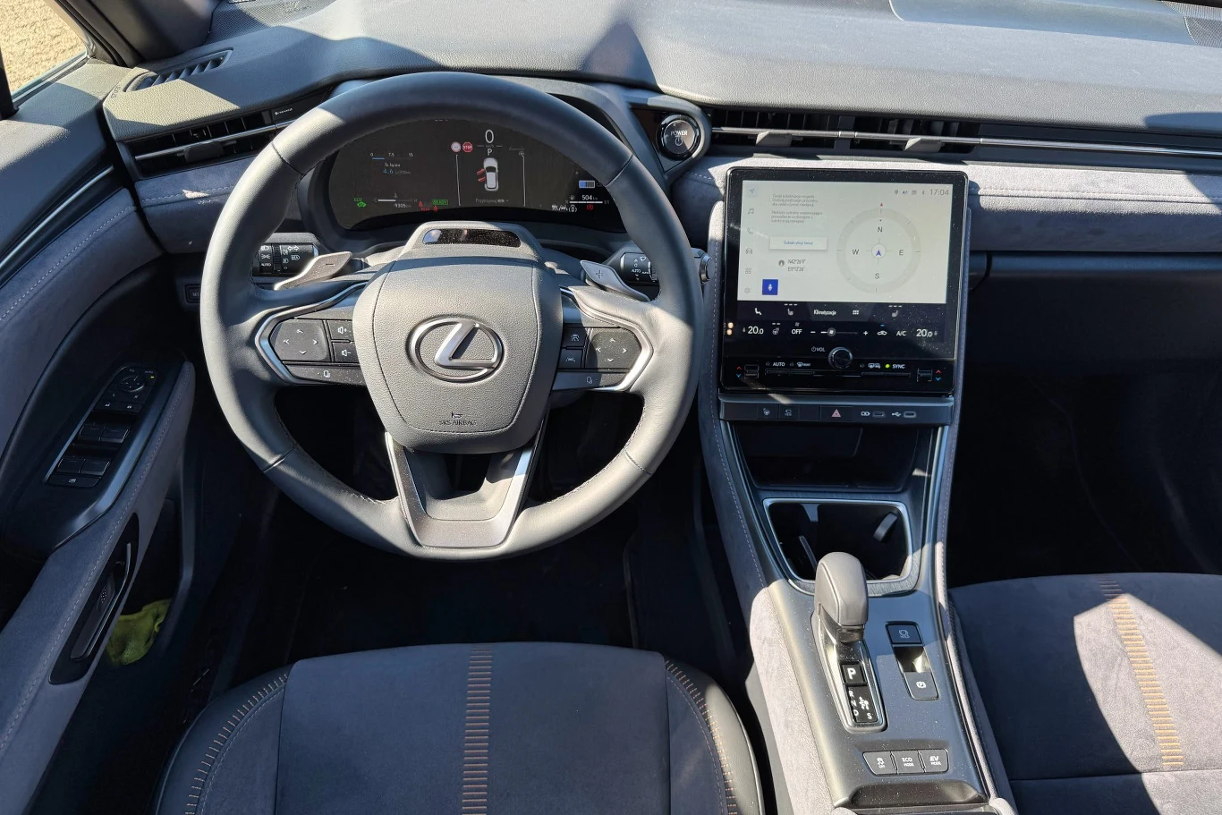 Nowoczesne wnętrze samochodu marki Lexus z elektroniczną deską rozdzielczą, dużym ekranem centralnym dotykowym oraz skórzaną kierownicą. Całość utrzymana w eleganckiej, stonowanej kolorystyce.