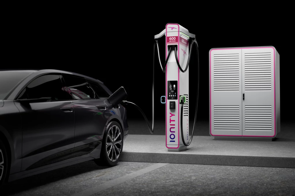 HYC1000 składa się z DC + Power Cabinet. Samochód elektryczny podłączony do stacji ładowania Ionity na tle ciemnego otoczenia, obok widoczna jest szafa techniczna związana z infrastrukturą ładowania.