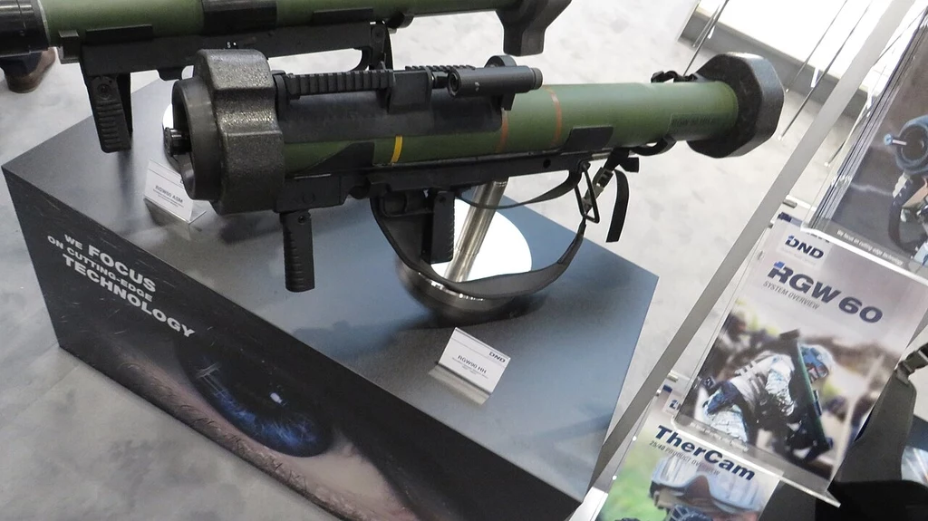 Granatnik RGW-90 Wyrzutnia przeciwpancerna na ekspozycji, zamocowana na podstawce do prezentacji, otoczona tabliczkami informacyjnymi i materiałami promocyjnymi producenta.