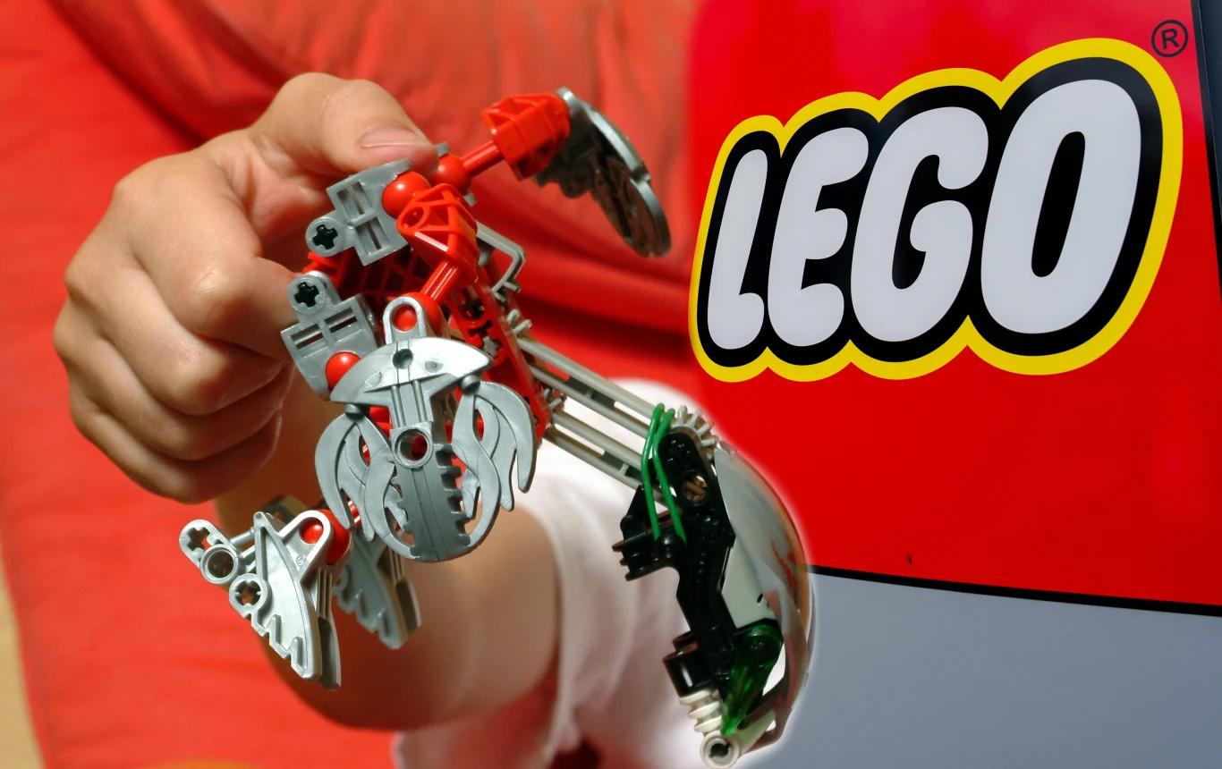 Masks of Power zapowiadała się na prawdziwy hit w uniwersum LEGO Osoba trzyma model figurki LEGO Bionicle na tle dużego, czerwonego opakowania z widocznym logo LEGO.