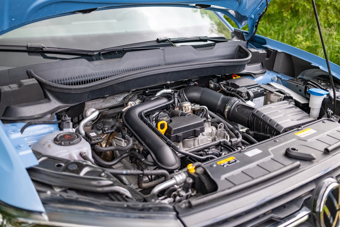 Otwarta maska samochodu ukazująca szczegółowo silnik, przewody, akumulator oraz inne elementy mechaniczne w dobrze doświetlonym otoczeniu.