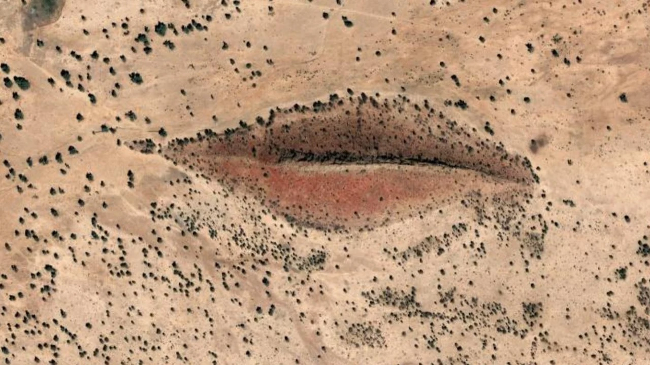 „Usta” w Sudanie na zdjęciu z Google Earth Formacja ziemna przypominająca kształtem oko, otoczona suchym, piaszczystym terenem z rzadką roślinnością i pojedynczymi krzewami.
