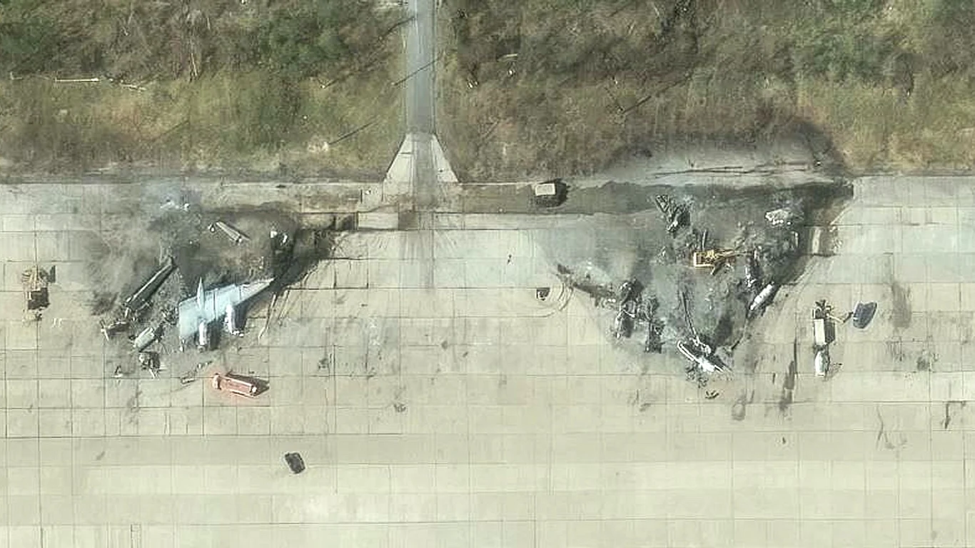 Zdjęcia satelitarne ukazują koszmarne straty w lotnictwie Rosji Dwa zniszczone samoloty wojskowe leżą rozbite na płycie lotniska, wokół widoczne ślady pożaru i zniszczeń, całość otoczona przez betonowe podłoże i niewielką roślinność wokół lotniska.