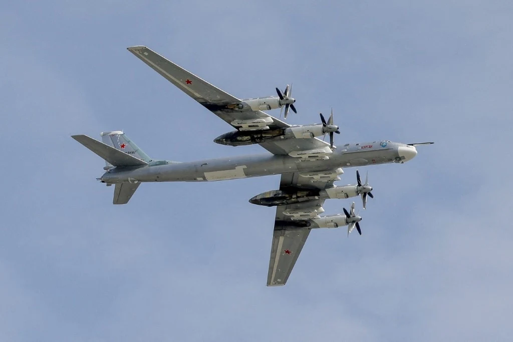 Rosyjski bombowiec strategiczny Tu-95 Wojskowy samolot strategiczny z charakterystycznym napędem śmigłowym, widoczny w locie na tle błękitnego nieba, z wyraźnie oznaczoną czerwonymi gwiazdami przynależnością państwową.