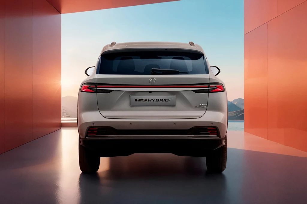 Nowy MG HS Hybrid+ będzie dostępny na polskim rynku w dwóch opcjach wyposażenia: Excite i Exclusive. Biały samochód hybrydowy marki MG HS widziany od tyłu, ustawiony pomiędzy dwoma nowoczesnymi, czerwonymi ścianami z panoramą górską i zachodzącym słońcem w tle.