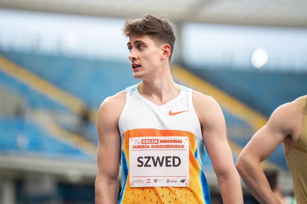 Maksymilian Szwed Młody mężczyzna w sportowym stroju z numerem startowym SZWED, znajdujący się na stadionie, w tle widoczne trybuny i fragment innej osoby.