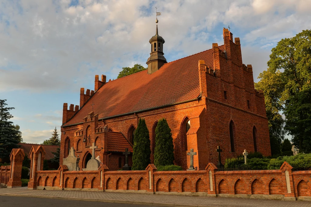Katedra w Pelplinie to jeden z największych gotyckich kościołów w Polsce Zabytkowy kościół z czerwonej cegły otoczony niskim murem, z wieżyczką zwieńczoną krzyżem, w otoczeniu zieleni i kilku rzeźb nagrobnych.