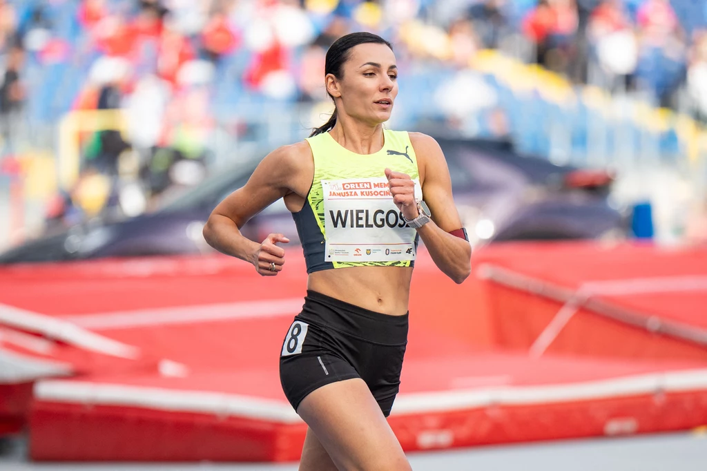 Anna Wielgosz Atletka w żółtym stroju sportowym biegnie po bieżni stadionu, z numerem startowym przypiętym do koszulki, w tle widoczne trybuny i rozmazani kibice.