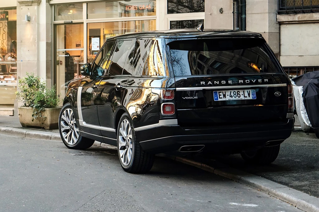 Duże SUV-y niosą ze sobą poważne zagrożenia. Czarny Range Rover Vogue zaparkowany na poboczu miejskiej ulicy, w tle witryny sklepów i elewacje budynków.
