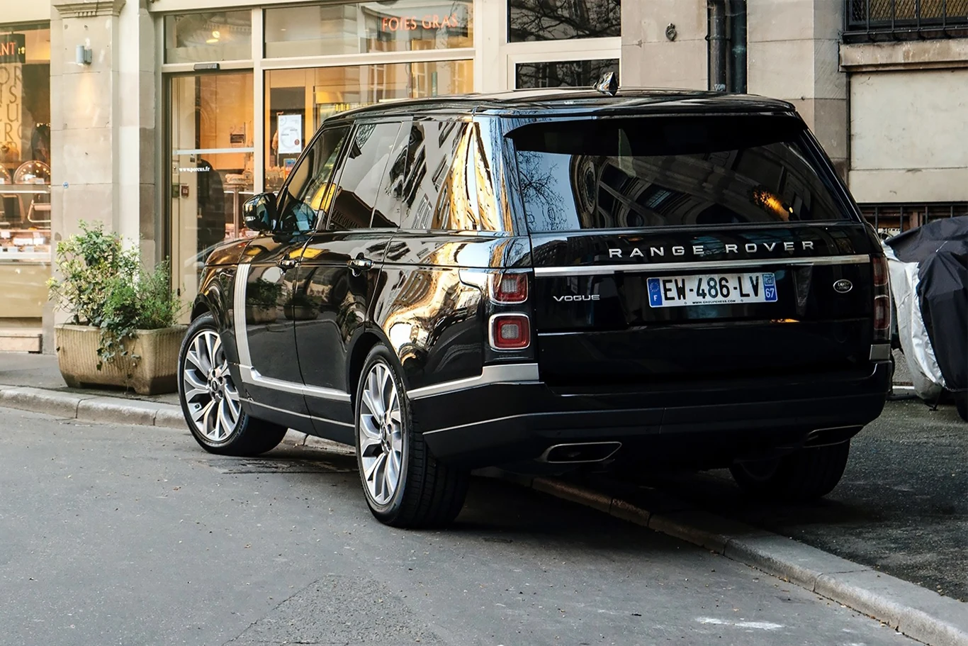 Czarny Range Rover Vogue zaparkowany na poboczu miejskiej ulicy, w tle witryny sklepów i elewacje budynków.