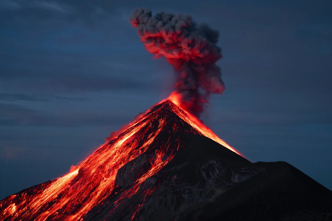 Wybuch wulkanu Fuego w Gwatemali Aktywny wulkan wyrzucający gorące strumienie lawy oraz kłęby czarnego dymu pod osłoną zmierzchu.