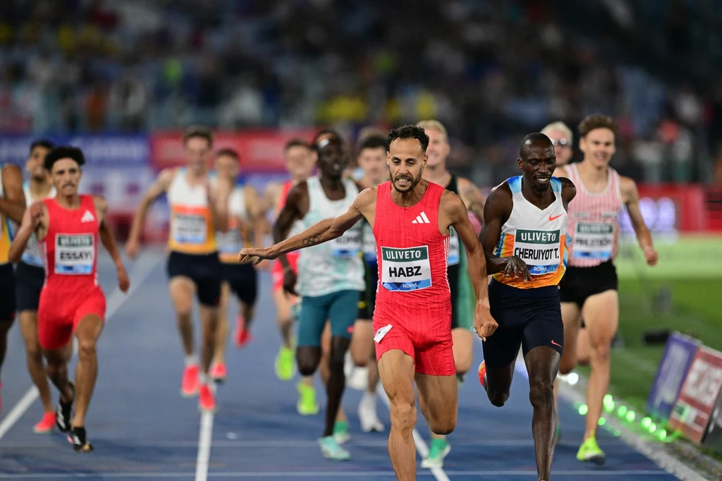 Azeddine Habz lepszy w DL w Rzymie od Timoty'ego Cheruyota. A Filip Rak z tyłu, przy krawężnika. Z rekordem życiowym Dwóch zawodników na czele wyścigu lekkoatletycznego finiszuje na bieżni, w tle kilku biegaczy, dynamiczna atmosfera zawodów sportowych, widoczne emocje i napięcie na twarzach sportowców.