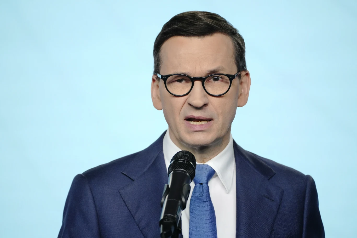 Mateusz Morawiecki ostrzega przed rosyjską dezinformacją Mężczyzna w okularach i garniturze przemawia do mikrofonu na jasnym tle.