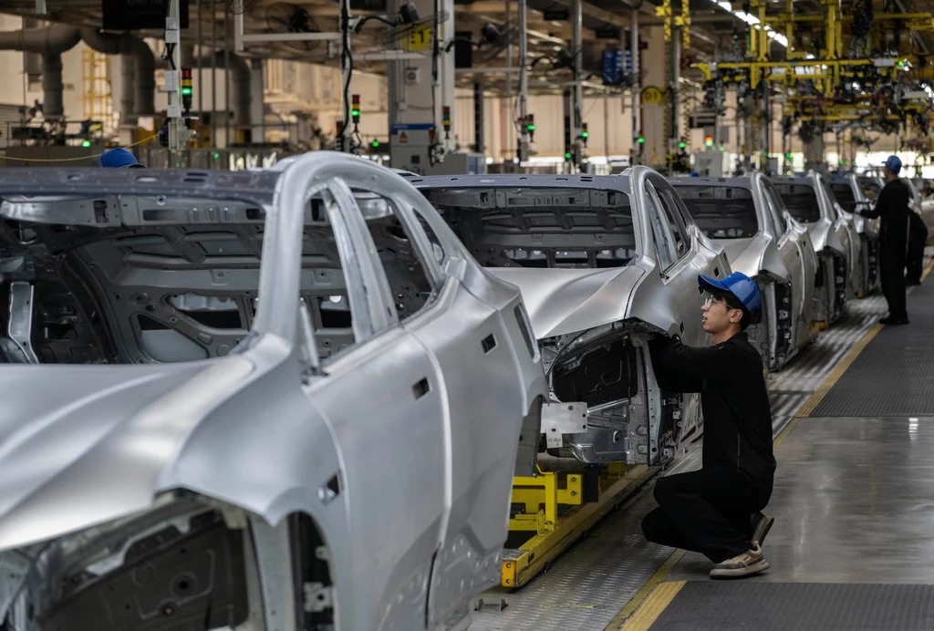 Chiny wciąż są kluczowym emitentem dwutlenku węgla Pracownik w czapce z daszkiem montuje karoserię samochodu na linii produkcyjnej w dużej hali fabrycznej, wokół znajdują się kolejne karoserie ustawione w szeregu gotowe do dalszego montażu.