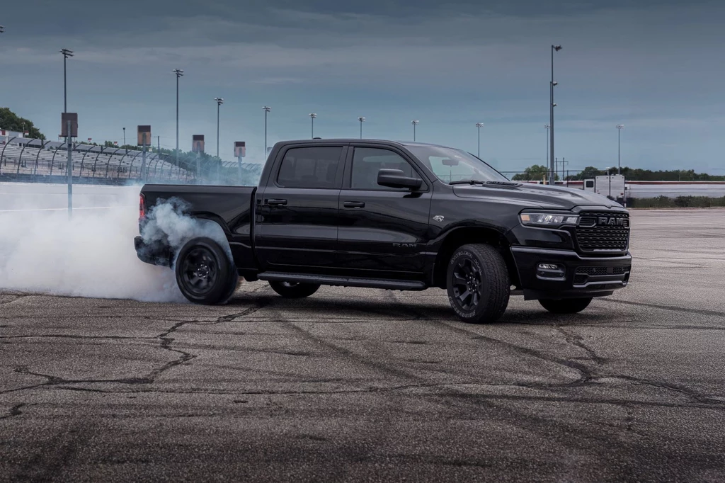 Silnik V8 wróci pod maskę RAM-a Czarny pickup marki RAM na torze, tylne koła generują dym podczas gwałtownego przyspieszenia lub driftu, asfalt z wyraźnymi śladami opon, w tle barierki toru oraz słupy oświetleniowe pod pochmurnym niebem.