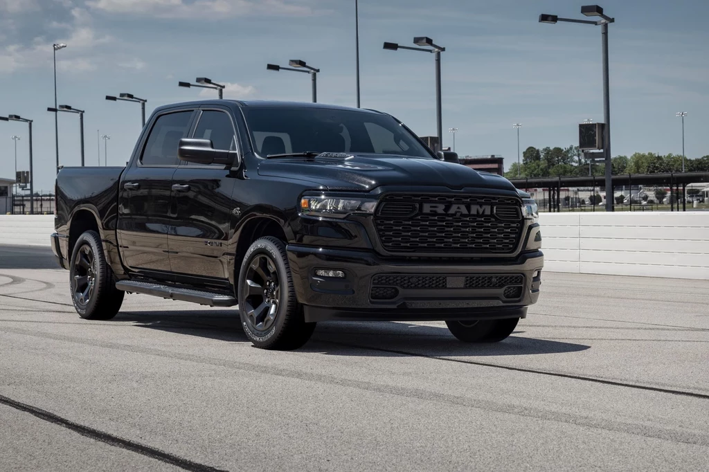 RAM 1500 znowu dostępny z silnikiem V8 Czarny pickup RAM zaparkowany na torze wyścigowym, w otoczeniu wysokich lamp i barier ochronnych, z wyraźnie widocznymi detalami karoserii oraz felgami w czarnym kolorze.