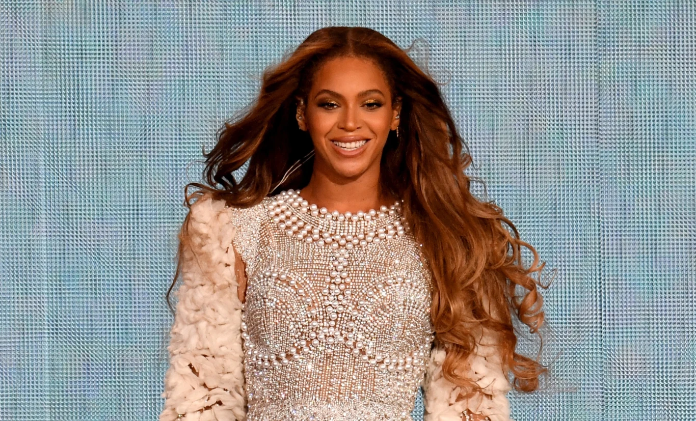 Beyonce szybko opanowała kryzysową sytuację na scenie Uśmiechnięta kobieta z długimi, brązowymi włosami nosi bogato zdobioną, cekinową suknię z perełkami na tle jasnego, błyszczącego ekranu.