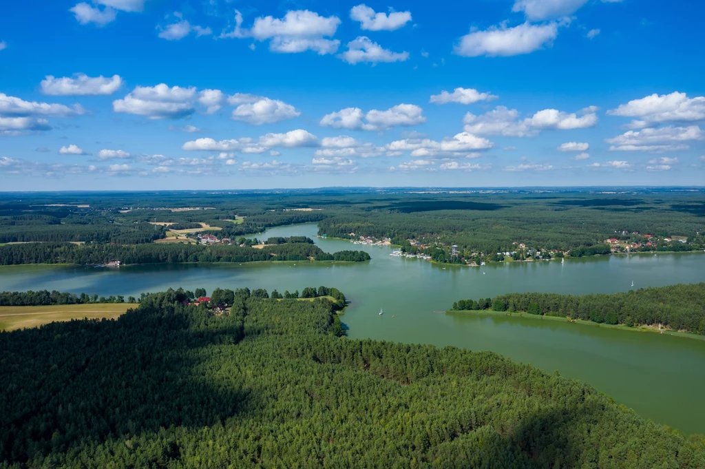 Układ jezior przypominający krzyż to wizytówka Wdzydzkiego Parku Krajobrazowego. Czekają tu spektakularne widoki i tereny rekreacyjne Rozległe jezioro otoczone gęstymi lasami oraz niewielkimi miejscowościami pod błękitnym niebem z rozproszonymi chmurami, wyraźny podział linii brzegowej i naturalny krajobraz.
