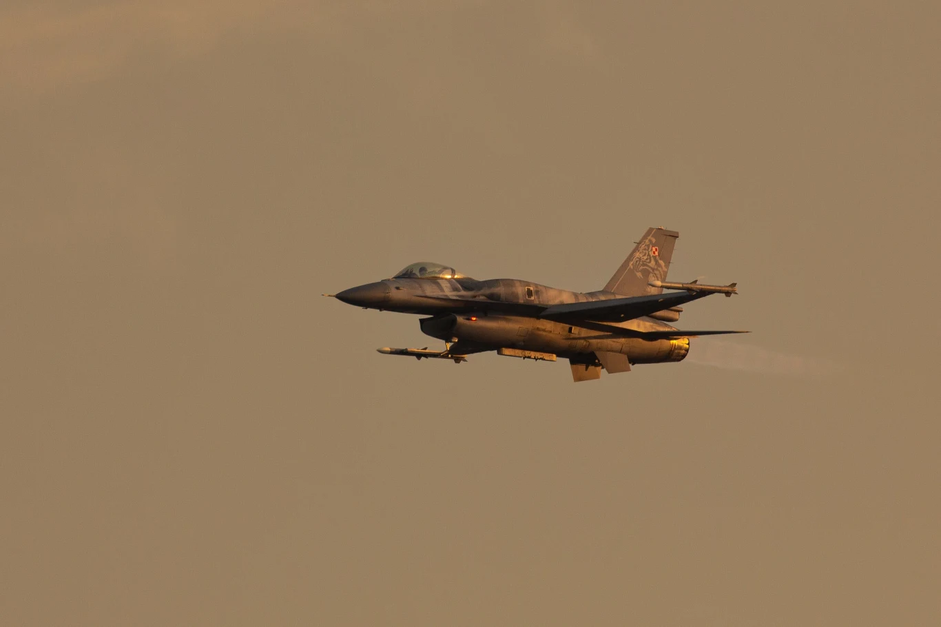 Rosjanie zaatakowali Ukrainę. Odpowiedź polskiego wojska, poderwano myśliwce, zdj. ilustracyjne Samolot myśliwski lecący na tle nieba w ciepłym świetle, widoczne uzbrojenie pod skrzydłami, maszyna w ujęciu bocznym w trakcie lotu.