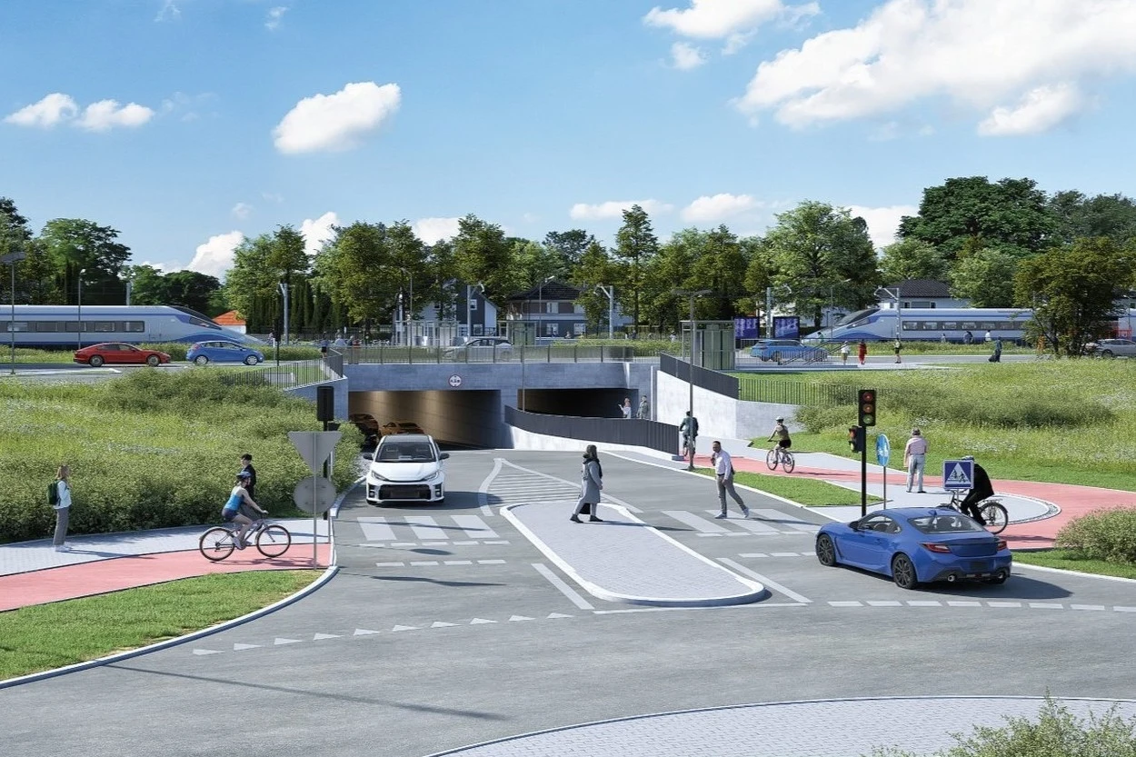 W Warszawie rozpoczyna się ważnego tunelu. 180 m będzie kosztować przeszło 90 mln zł./wizualizacja/ Nowoczesne skrzyżowanie z tunelu pod torami kolejowymi, samochody, rowerzyści i piesi korzystający z przejścia, sygnalizacja świetlna, tory kolejowe oraz pociągi w tle, otoczenie zielenią miejską.