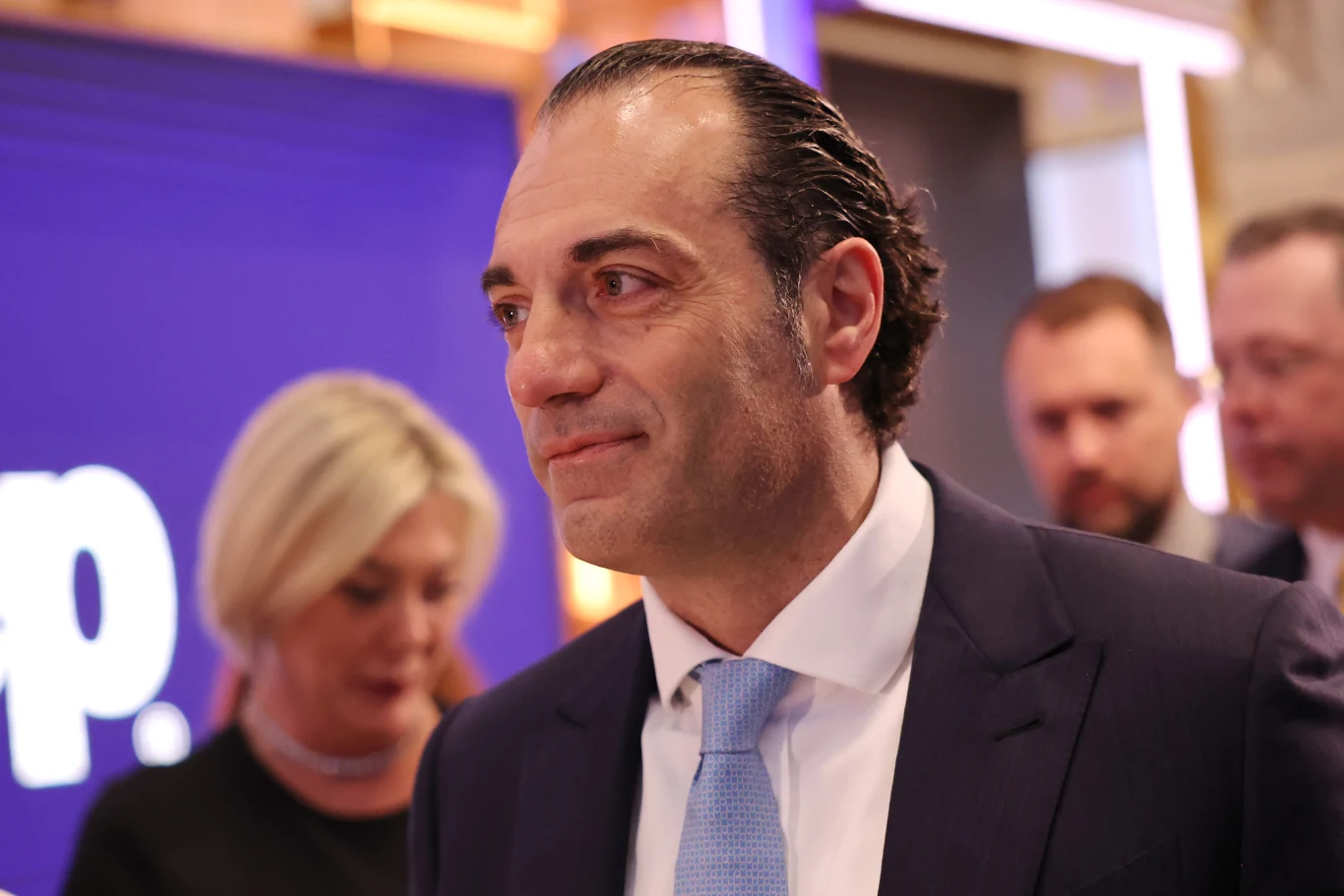 Niemal 10,2 mln dolarów rocznie. Tyle otrzyma nowy dyrektor Stellantisa Uśmiechnięty mężczyzna w garniturze z niebieskim krawatem, stojący na tle rozmytych osób w formalnych strojach, w jasnym, eleganckim wnętrzu.