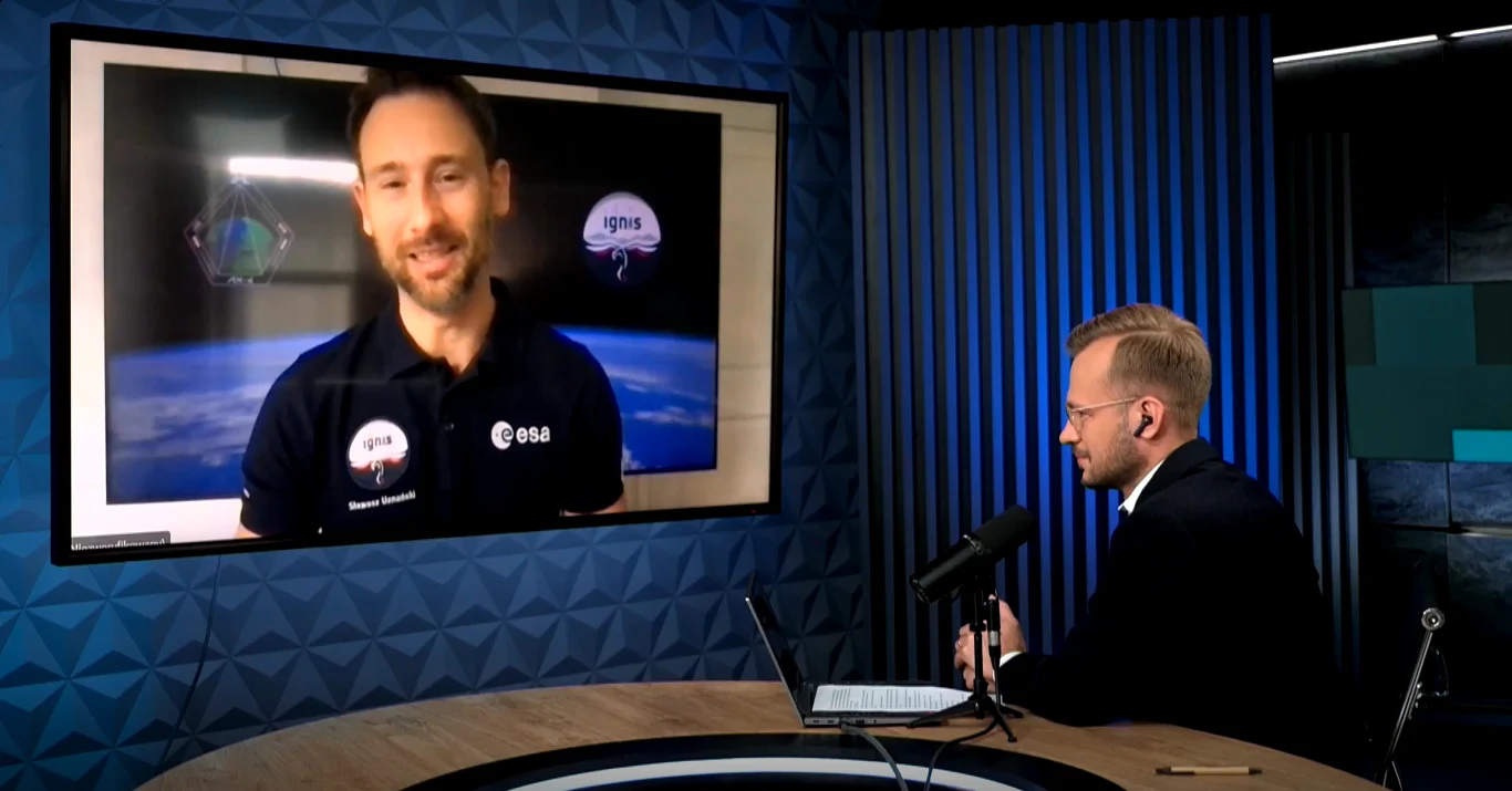 Polski astronauta Sławosz Uznański-Wiśniewski opowiada o swojej perspektywie lotu na Międzynarodową Stację Kosmiczną. Rozmowa prowadzona online, po lewej stronie ekran z transmisją wideo z mężczyzną w koszulce ESA na tle symulacji Ziemi, po prawej stronie mężczyzna przy mikrofonie w nowoczesnym studiu nagraniowym.