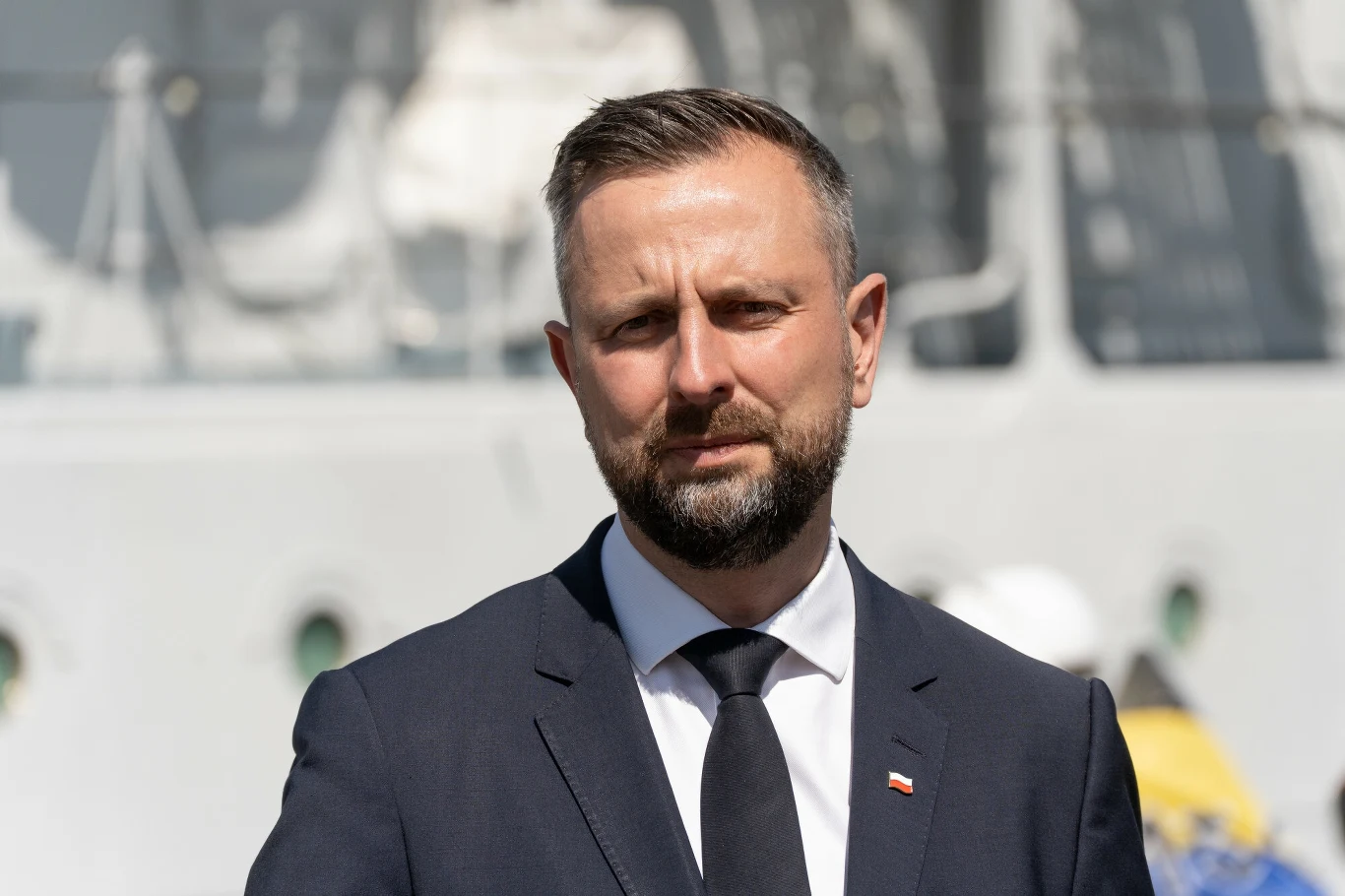 Władysław Kosiniak-Kamysz apeluje ws. wyników wyborów prezydenckich Mężczyzna w garniturze i krawacie stoi na tle dużego statku, na klapie marynarki ma przypiętą flagę Polski.