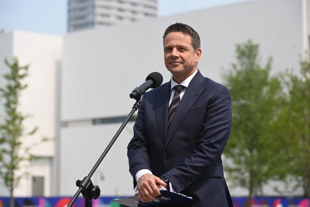 Rafał Trzaskowski przegrał wybory prezydenckie. Marek Sawicki tłumaczy przyczyny porażki Mężczyzna w garniturze przemawia do mikrofonu na tle nowoczesnych budynków i zieleni.