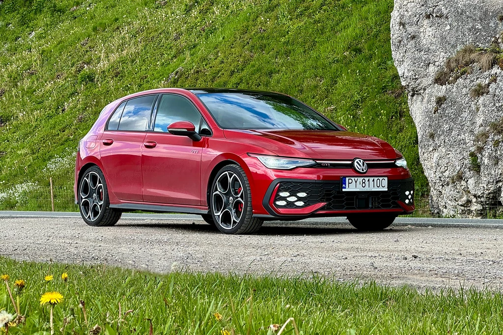 Volkswagen wysłuchał opinii klientów i w odświeżonej wersji sportowego Golfa wprowadził sporo poprawek. Czerwony Volkswagen Golf GTI zaparkowany na drodze asfaltowej obok zielonego zbocza z dużym wapiennym głazem, na pierwszym planie widoczna trawa i żółte kwiaty.