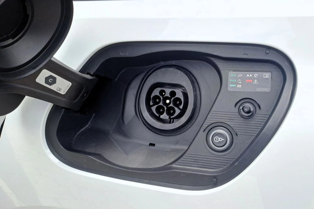 Akumulator o pojemności 20,7 kWh netto można ładować prądem o mocy 11 kW. Gniazdo ładowania samochodu elektrycznego z widocznym portem oraz panelem sterowania i przyciskiem uruchamiania.