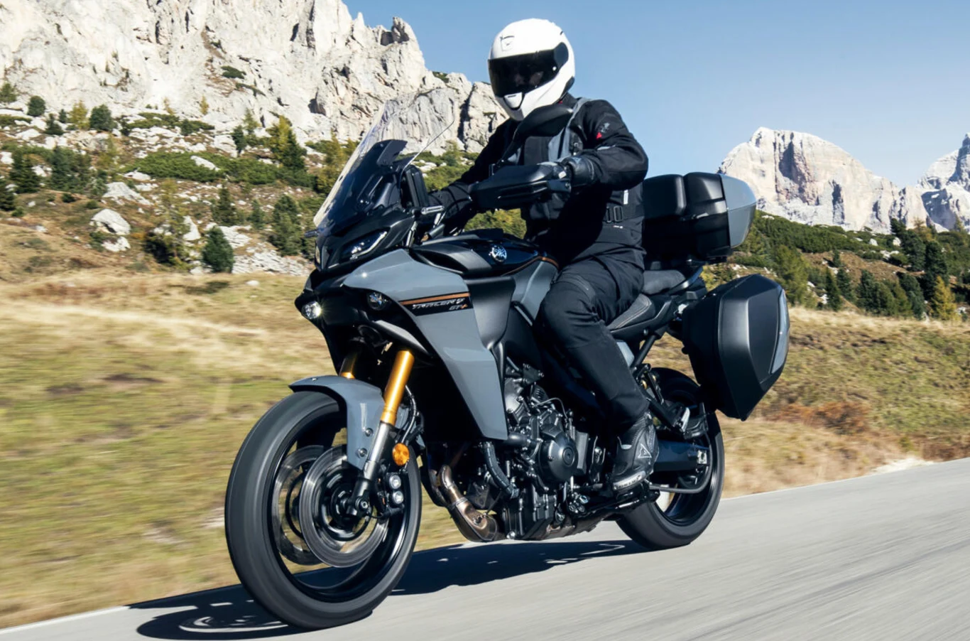 Yamaha Tracer 9 GT wyposażona jest w kufry z technologią bezstykową. Motocyklista w pełnym stroju ochronnym jadący nowoczesnym motocyklem turystycznym po asfaltowej drodze, w tle górski krajobraz z wapiennymi skałami oraz niską roślinnością.