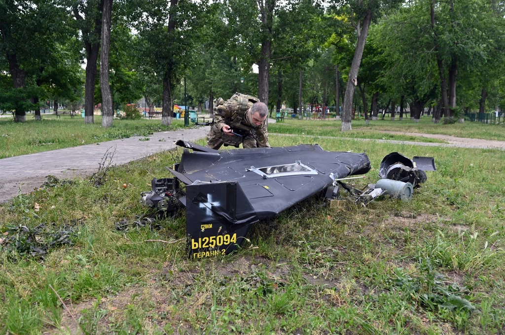 Wrak bezzałogowca Szahed-136 o rosyjskim oznaczeniu Gerań-2 Rozbity wrak drona wojskowego leżący na trawie w parku, zbliżony żołnierz w mundurze przygląda się szczątkom, w tle widoczne drzewa i ścieżki parkowe.