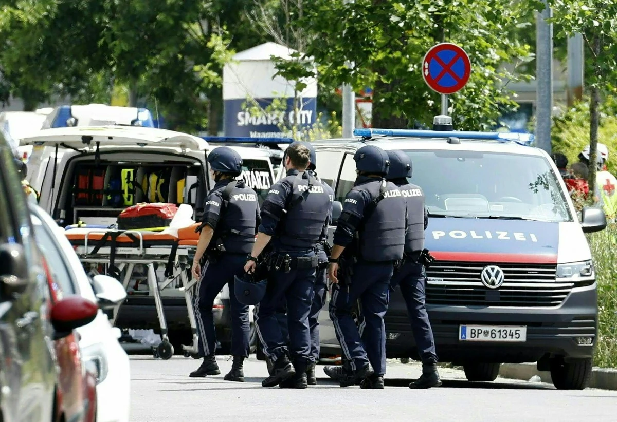 W szkole w austriackim mieście Graz doszło do strzelaniny Czterech uzbrojonych funkcjonariuszy policji w mundurach i kamizelkach kuloodpornych stoi przy ambulansie i radiowozie, jeden z ratowników przygotowuje nosze medyczne, w tle widoczne zaparkowane samochody i drzewa.