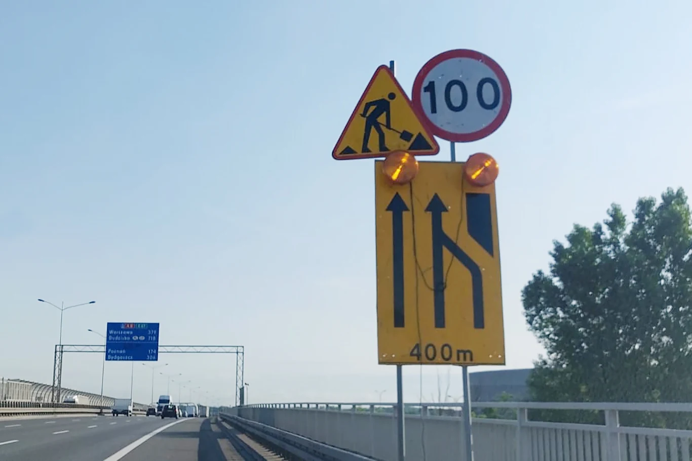 Ważny remont obwodnicy Wrocławia wstrzymany | Fot. Jacek Ostruszka Zestaw znaków drogowych informujących o prowadzeniu prac drogowych na autostradzie, ograniczeniu prędkości do 100 km/h oraz o zwężeniu pasa ruchu za 400 metrów; asfaltowa jezdnia, barierki i tablica informacyjna widoczne na tle jasnego nieba.