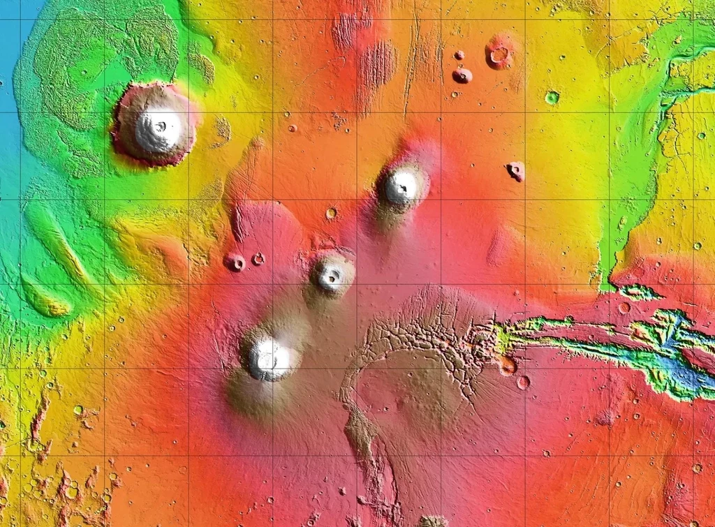 Łańcuch wulkaniczny Tharsis Montes na topograficznej mapie Marsa. Arsia Mons znajduje się najniżej. Ten po lewej to Olympus Mons, najwyższy wulkan w Układzie Słonecznym Kolorowa mapa topograficzna przedstawiająca obszar z wyraźnie zaznaczonymi wzniesieniami i depresjami, dominantą są cztery duże wulkany otoczone mniejszymi formacjami terenu.