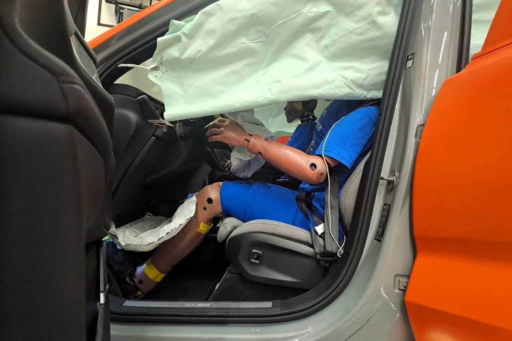 Na podstawie zebranych danych Volvo zadeklarowało, że pasażerowie biorący udział w takim zdarzeniu, jakie nam zaprezentowano, nie odnieśliby żadnych poważnych obrażeń. Manekin w niebieskim ubraniu siedzi na miejscu kierowcy w samochodzie po wypadku. Przed manekinem znajduje się rozwinięta poduszka powietrzna. Drzwi samochodu są otwarte, a pomarańczowy element, prawdopodobnie służący do testów zderzeniowych, jest wido...