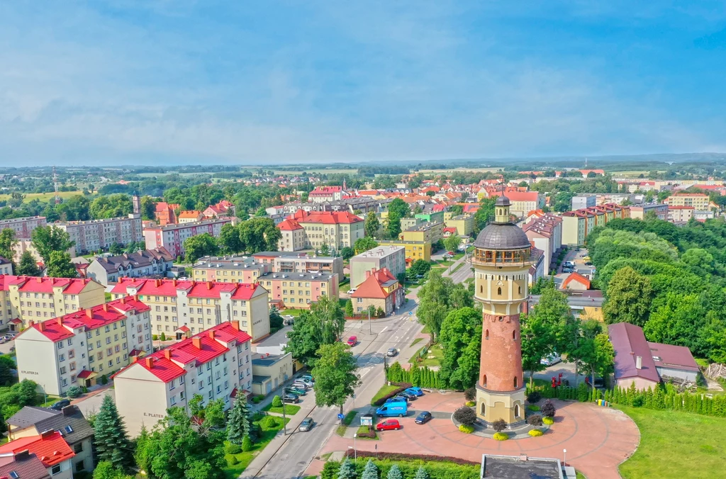 Widok z lotu ptaka na wieżę ciśnień w otoczeniu budynków mieszkalnych i zieleni w słoneczny dzień w mieście.