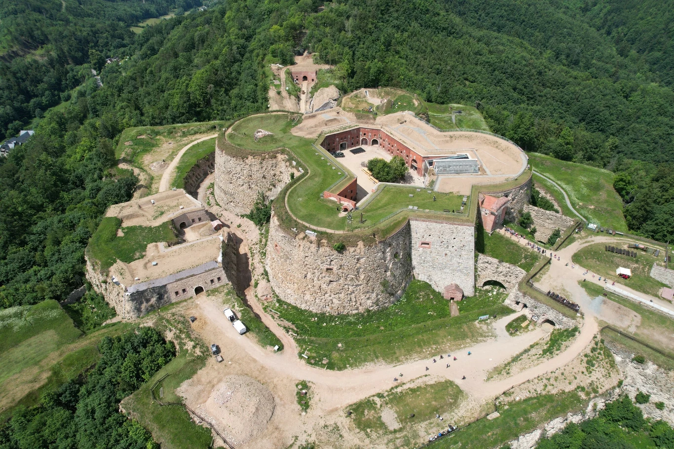 Jedna z najważniejszych atrakcji Dolnego Śląska Malownicza twierdza z masywnymi kamiennymi murami, otoczona zielonym wzgórzem i gęstymi lasami, widoczna z lotu ptaka, z wyraźnie zaznaczonymi bastionami, dziedzińcem i drogą prowadzącą do bramy.