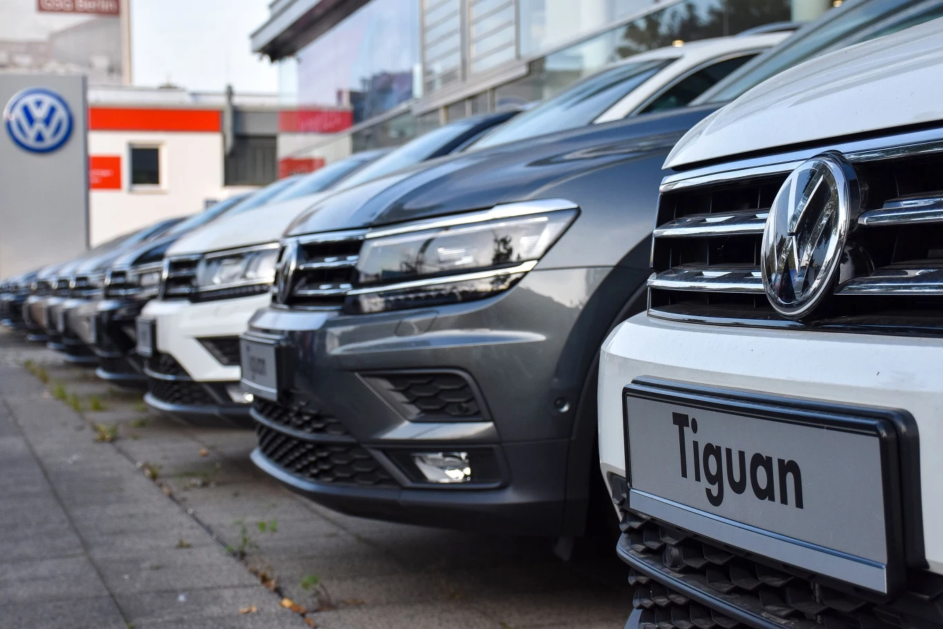 Volkswagen ostrzega przed oszustami, którzy oferują modele niemieckiej marki w bardzo korzystnych cenach Szereg nowych samochodów Volkswagen Tiguan ustawionych równolegle przed salonem samochodowym, z widocznymi tablicami rejestracyjnymi i logo marki.