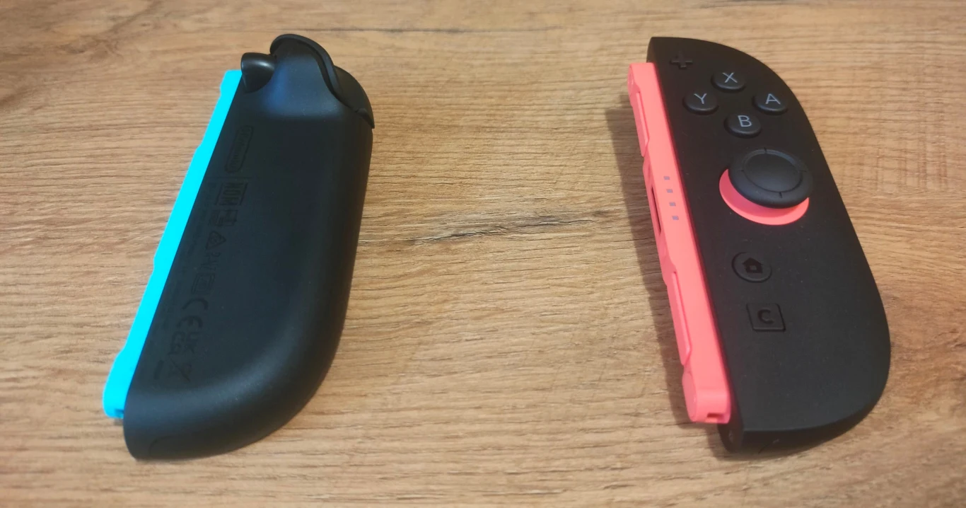 Dwa rozdzielone kontrolery do konsoli Nintendo Switch, jeden w kolorze niebieskim, drugi czerwonym, leżące na drewnianej powierzchni.