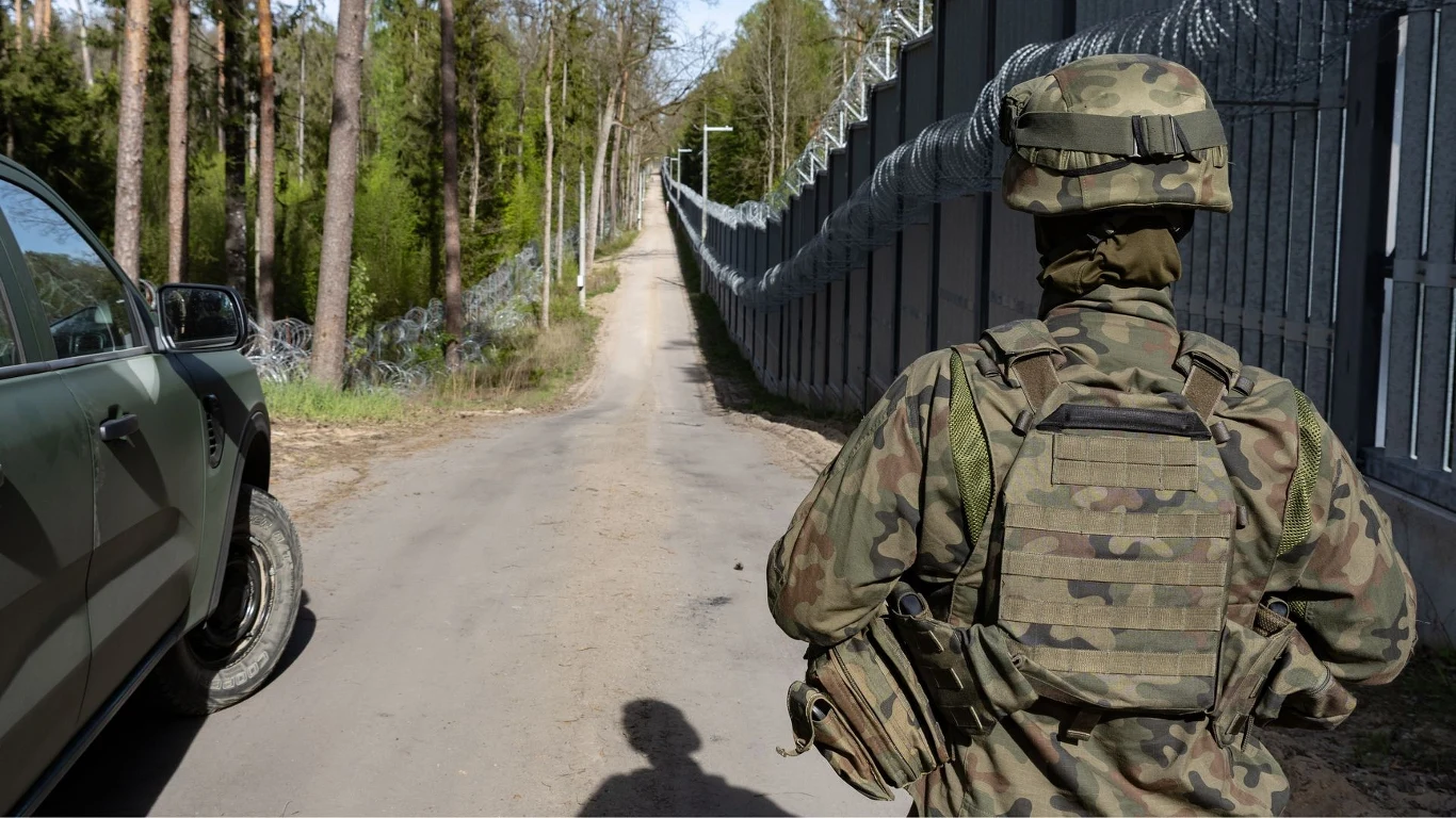Strzały na granicy polsko-białoruskiej. Jest akt oskarżenia dla żołnierza Żołnierz w mundurze polowym patroluje drogę biegnącą wzdłuż wysokiego ogrodzenia z drutem kolczastym, obok stoi wojskowy pojazd terenowy, w tle widoczny las.