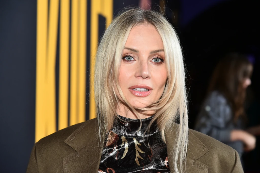 Agnieszka Woźniak-Starak żegna się z pracą w TVN Kobieta o blond włosach i jasnych oczach w brązowej marynarce oraz wzorzystej, aksamitnej bluzce na tle z żółtymi pionowymi napisami.