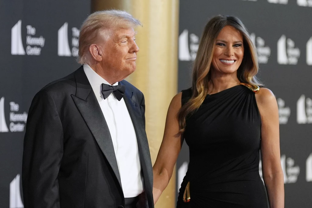 Gdy Donald i Melania Trumpowie pojawili się w Kennedy Center, zostali wygwizdani, a aktorzy odmówili udziału w przedstawieniu Para ubrana w eleganckie wieczorowe stroje stoi razem na tle ciemnej ściany z logotypami, kobieta uśmiecha się szeroko, a mężczyzna patrzy lekko w bok.