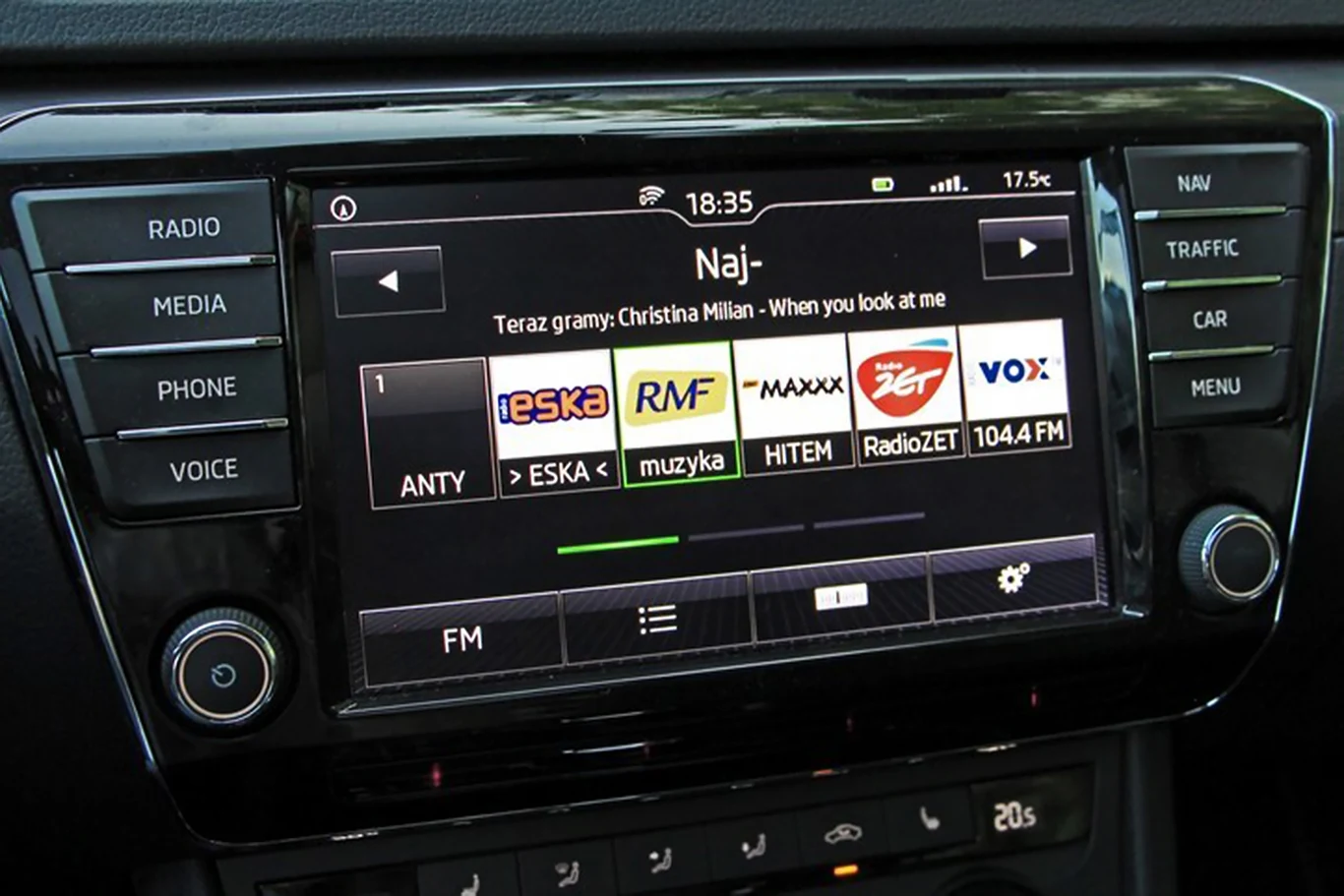 Opłaty obejmują nie tylko domowe odbiorniki, ale również radia w samochodach. Ekran radia samochodowego z interfejsem wyświetlającym stacje radiowe, aktualnie wybraną piosenkę oraz różne opcje sterowania dotykowego po bokach ekranu.