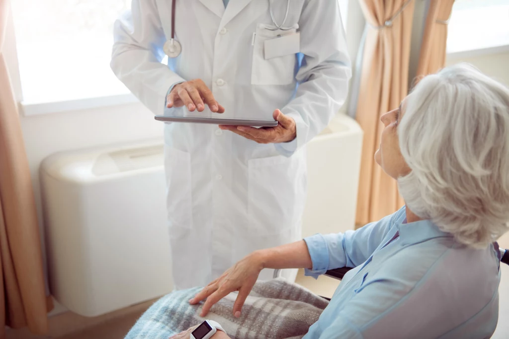 W przyszłości, diagnoza choroby Parkinsona zapewne będzie odbywać się przy udziale komputerów i sztucznej inteligencji Lekarz w białym kitlu korzysta z tabletu podczas rozmowy ze starszą kobietą siedzącą na wózku inwalidzkim, kobieta przykryta kocem, w dłoni trzyma smartfona.