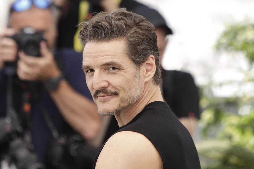 Kobiety mówią, że Pedro Pascal ma "to coś" Mężczyzna w czarnej koszulce patrzący przez ramię w stronę aparatu, w tle osoby z aparatami fotograficznymi wykonujące zdjęcia.