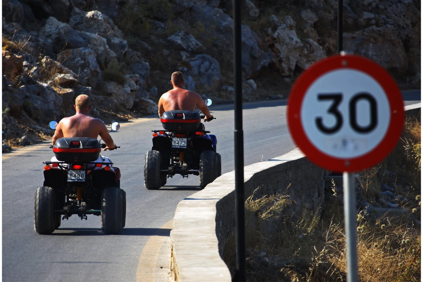 Zaostrzone przepisy będą dotyczyć zarówno mieszkańców, jak i turystów z zagranicy, którzy chętnie wypożyczają skutery i quady. Dwóch mężczyzn jadących na quadach po asfaltowej drodze wijącej się przez skalisty teren, przy drodze widoczny znak ograniczenia prędkości do 30 km/h